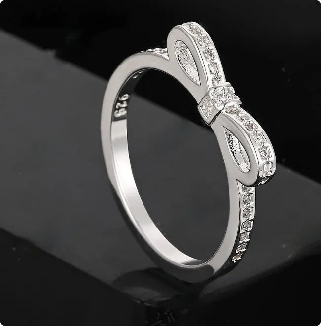Silver bow-shaped ring with rhinestone and zircon crystal details on a model finger.