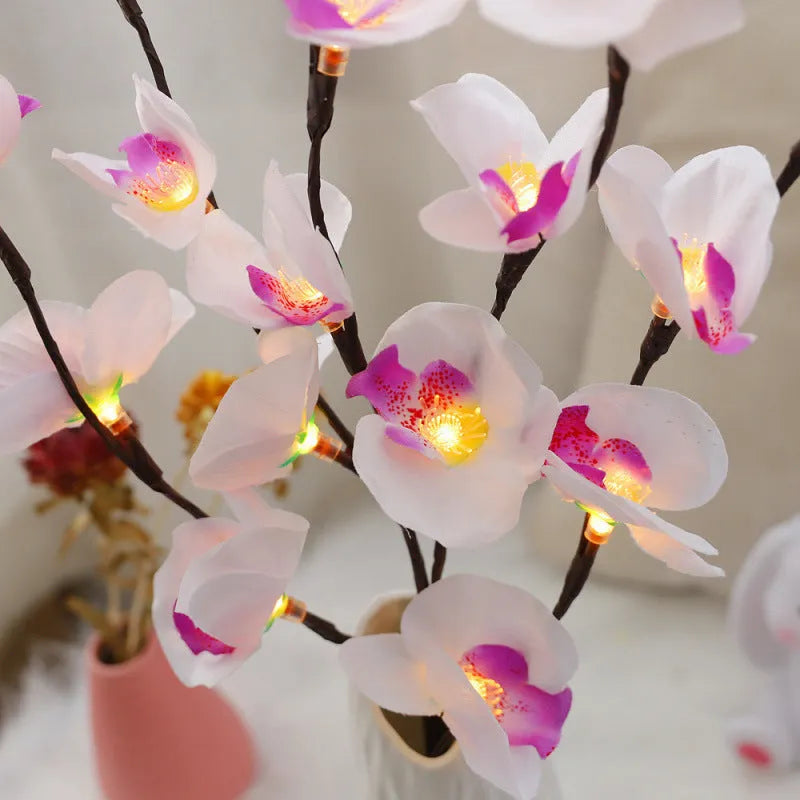 Pink artificial Phalaenopsis orchid branch LED decorative light, 65cm tall, on a bedside table.