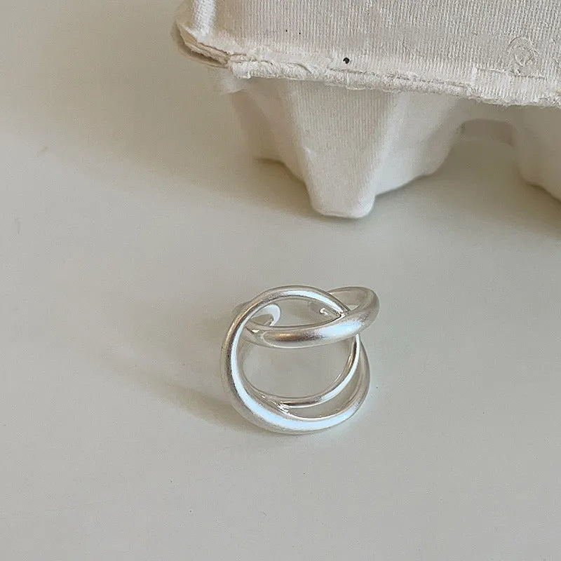 Geometric open ring with 3D interlaced matte metal design in gold or silver finish.