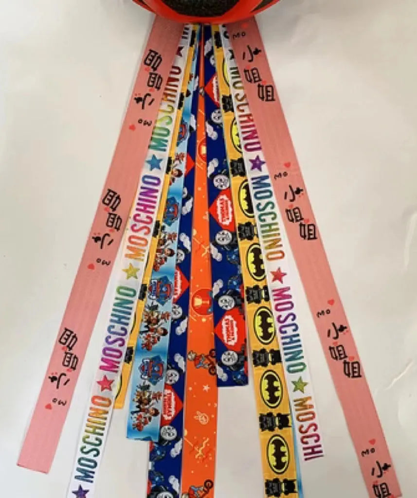 Colourful fabric helmet streamers for children's roller skating and ski helmets, shown in apricot, red, and grey.