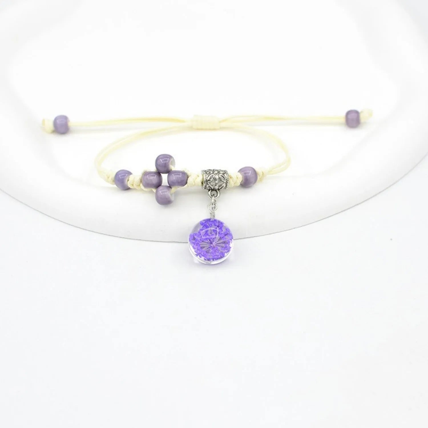 Close-up of a hand-woven glass bracelet with large beads containing real dried flowers and a lace design.