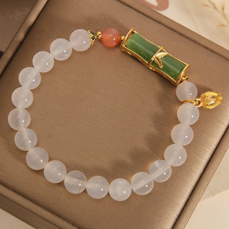 Close-up of a women's bracelet with a white agate jade bead and bamboo joint design on a natural background.