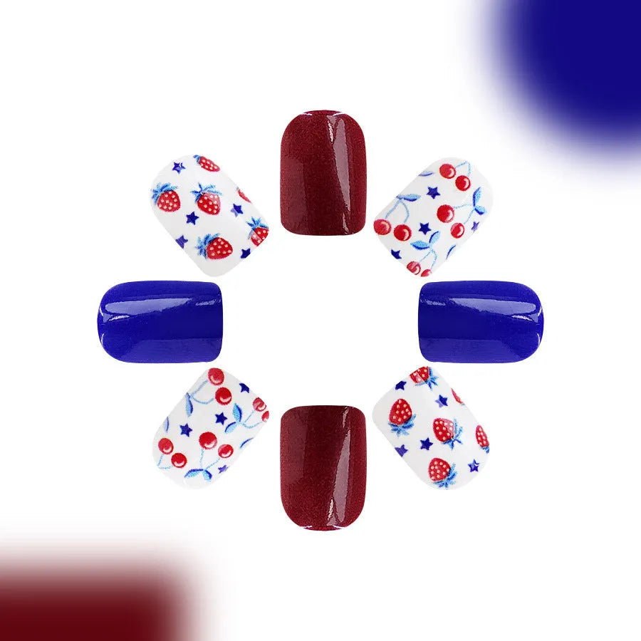 Short glossy false nails with strawberry and cherry pattern on red and blue background.