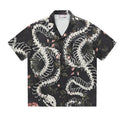 Man wearing a loose fit Cuban collar shirt with a printed snake bone and floral pattern in a summer setting.