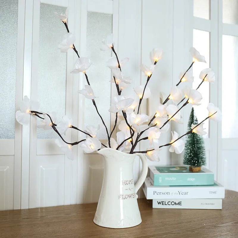 Pink artificial Phalaenopsis orchid branch LED decorative light, 65cm tall, on a bedside table.
