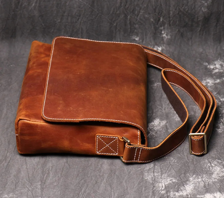 Men's vintage brown cowhide medium messenger bag showing front flap and long shoulder strap.