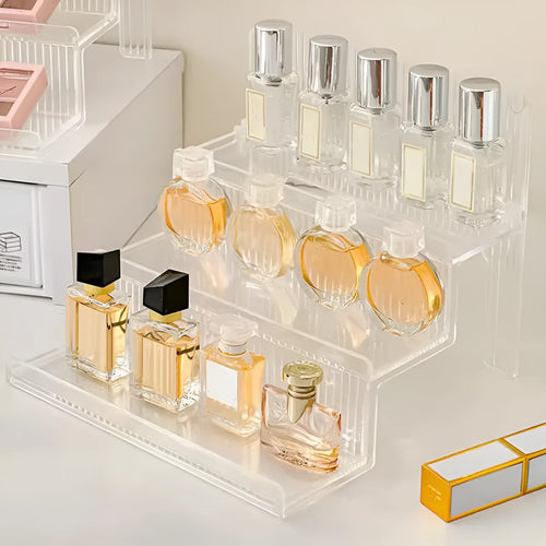 Transparent acrylic cosmetics storage rack with detachable shelves, displaying perfume bottles and small accessories