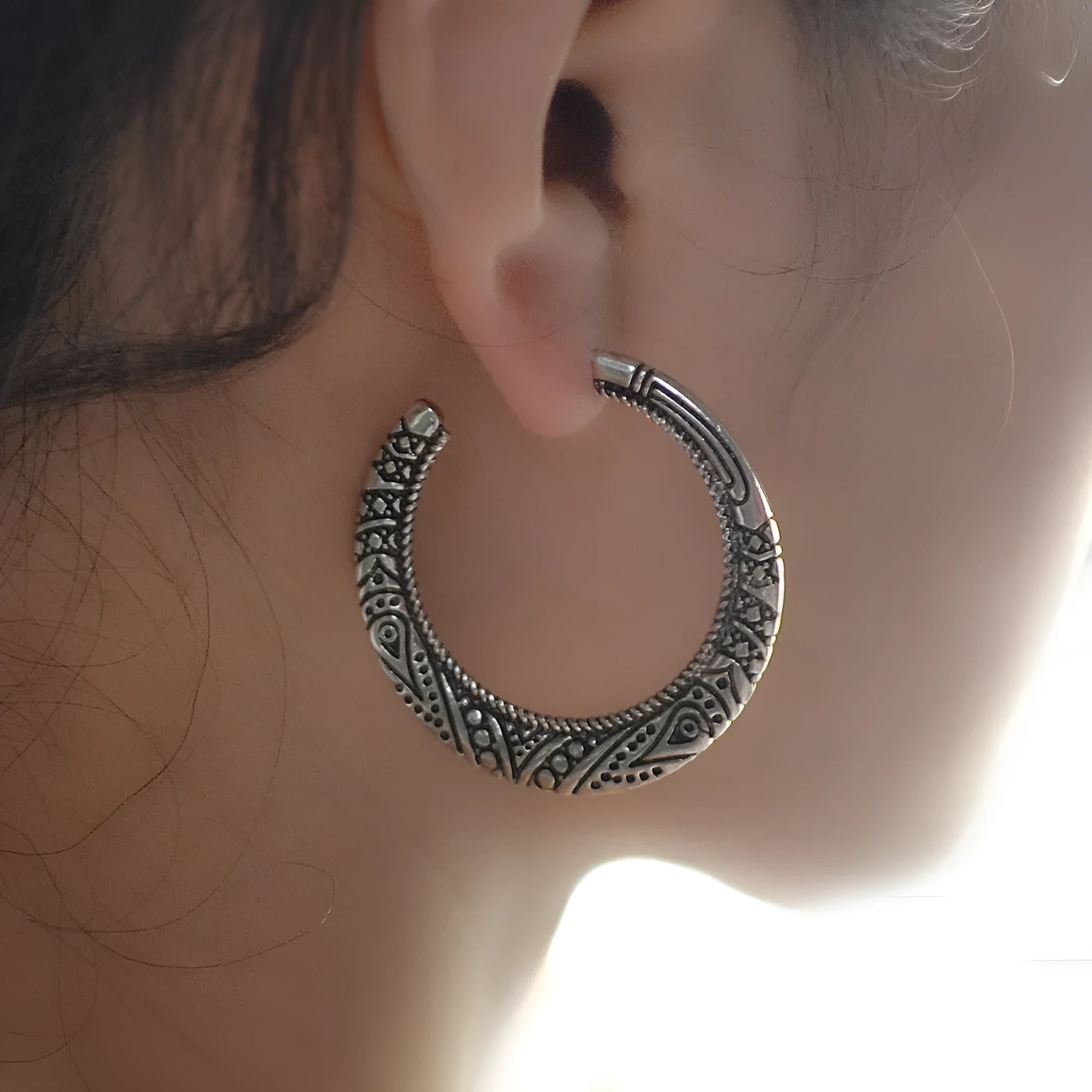 A pair of vintage-style C-shaped alloy earrings with detailed street shot engraving, shown in bronze finish.