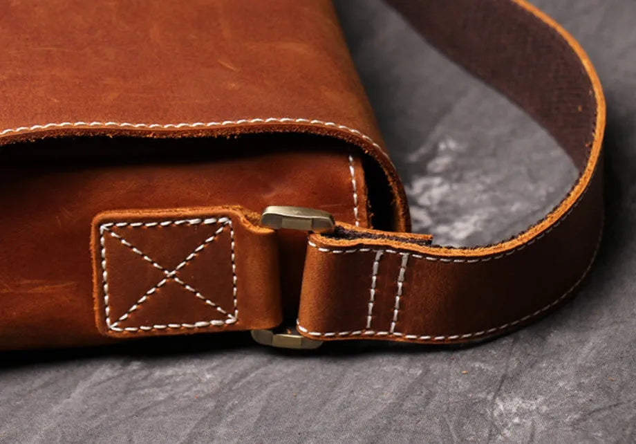 Men's vintage brown cowhide medium messenger bag showing front flap and long shoulder strap.