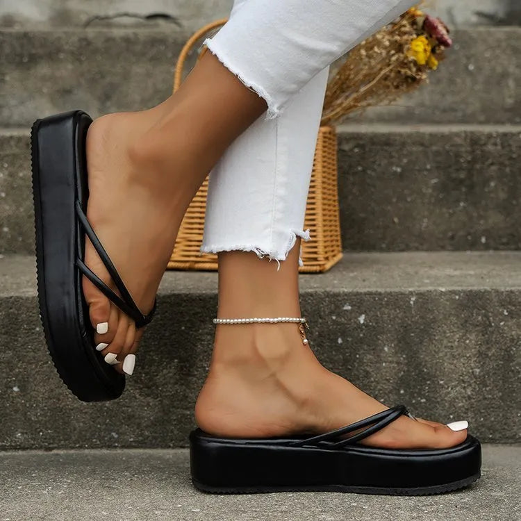 White thick-soled flip-flops with herringbone pattern PU upper and rubber sole on a sandy beach.