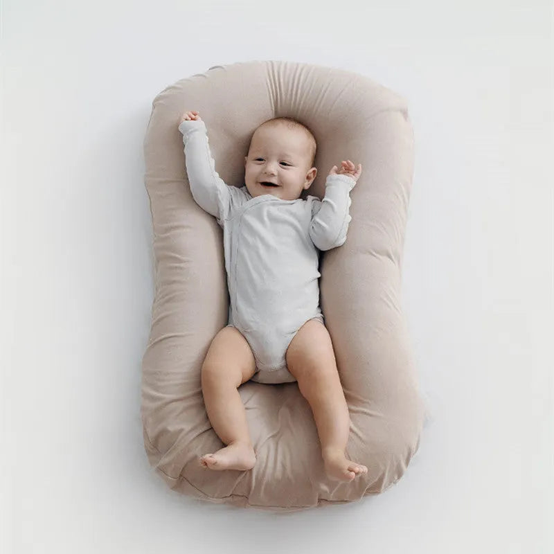 Beige portable baby nest crib for newborns measuring 75cm by 45cm on a neutral background.