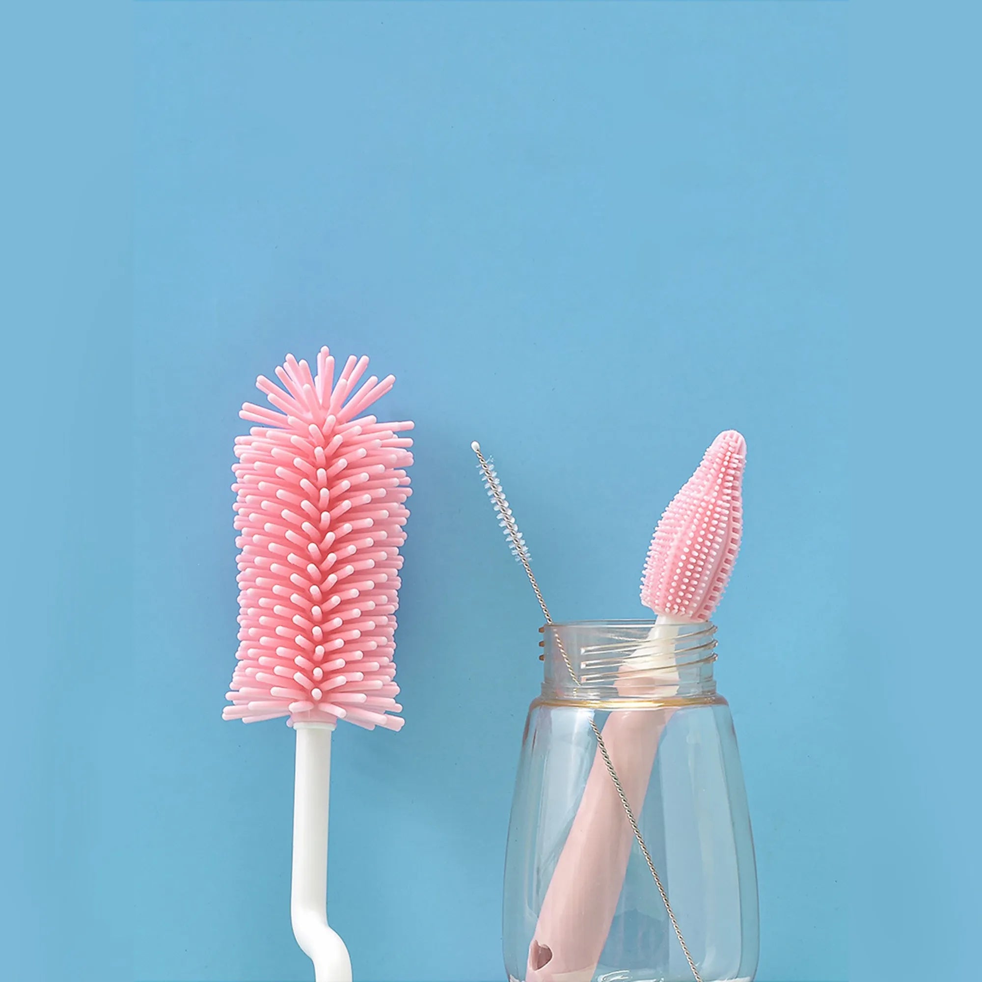 Blue, pink, and yellow silicone baby bottle brushes with an integrated straw cleaning tool.