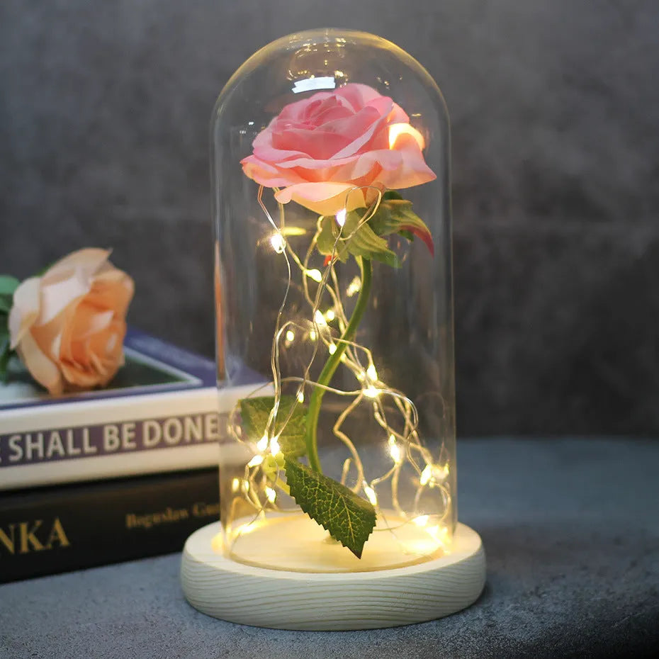 LED illuminated silk rose bouquet in a glass dome on a wooden base, with warm white lights.