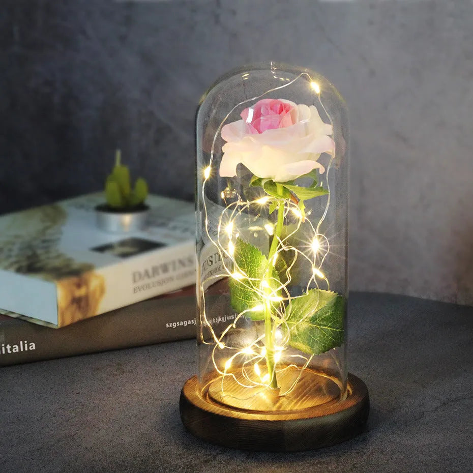 LED illuminated silk rose bouquet in a glass dome on a wooden base, with warm white lights.