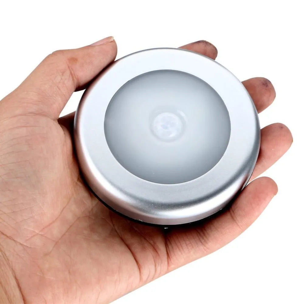 Silver circular battery-powered motion sensor night light on a surface.