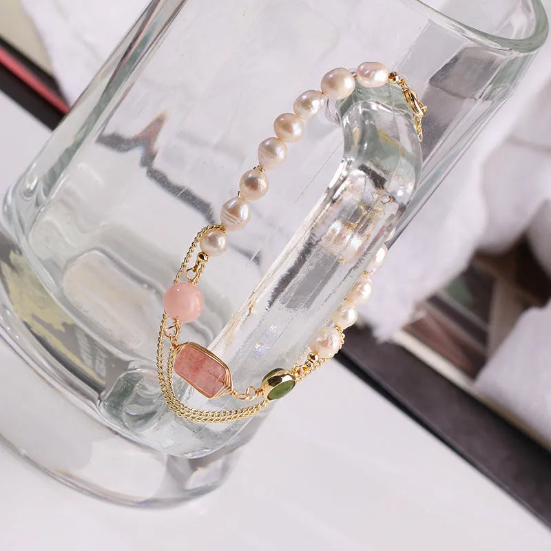Close-up of a women's bracelet with pink freshwater pearls and geometric strawberry crystal charms on a stainless steel chain.