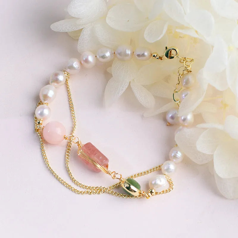 Close-up of a women's bracelet with pink freshwater pearls and geometric strawberry crystal charms on a stainless steel chain.