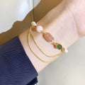 Close-up of a women's bracelet with pink freshwater pearls and geometric strawberry crystal charms on a stainless steel chain.