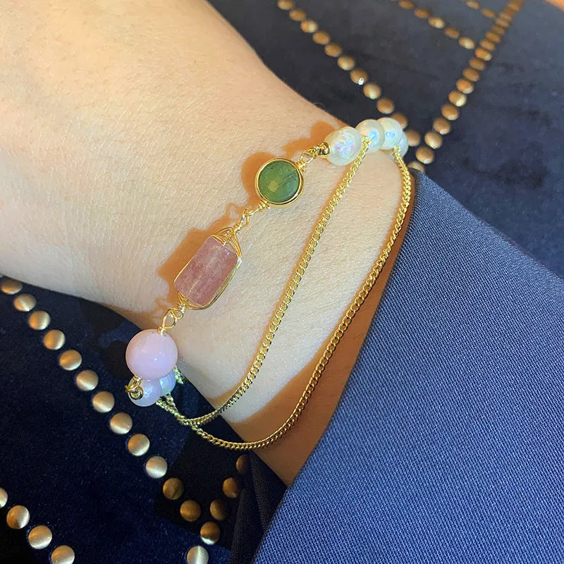 Close-up of a women's bracelet with pink freshwater pearls and geometric strawberry crystal charms on a stainless steel chain.