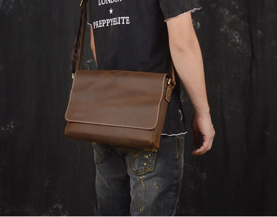 Men's vintage brown cowhide medium messenger bag showing front flap and long shoulder strap.