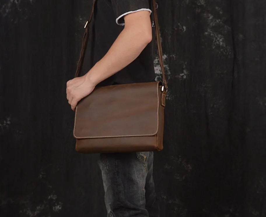 Men's vintage brown cowhide medium messenger bag showing front flap and long shoulder strap.
