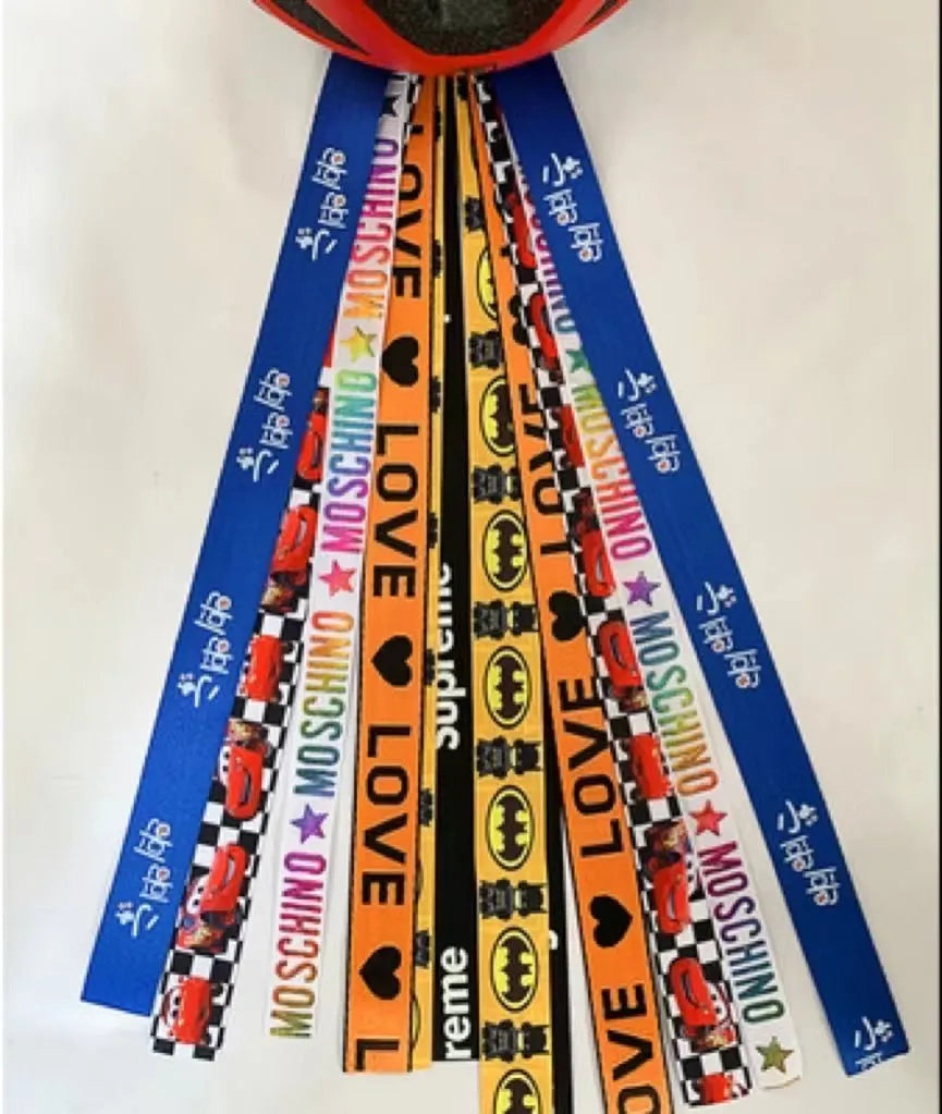 Colourful fabric helmet streamers for children's roller skating and ski helmets, shown in apricot, red, and grey.