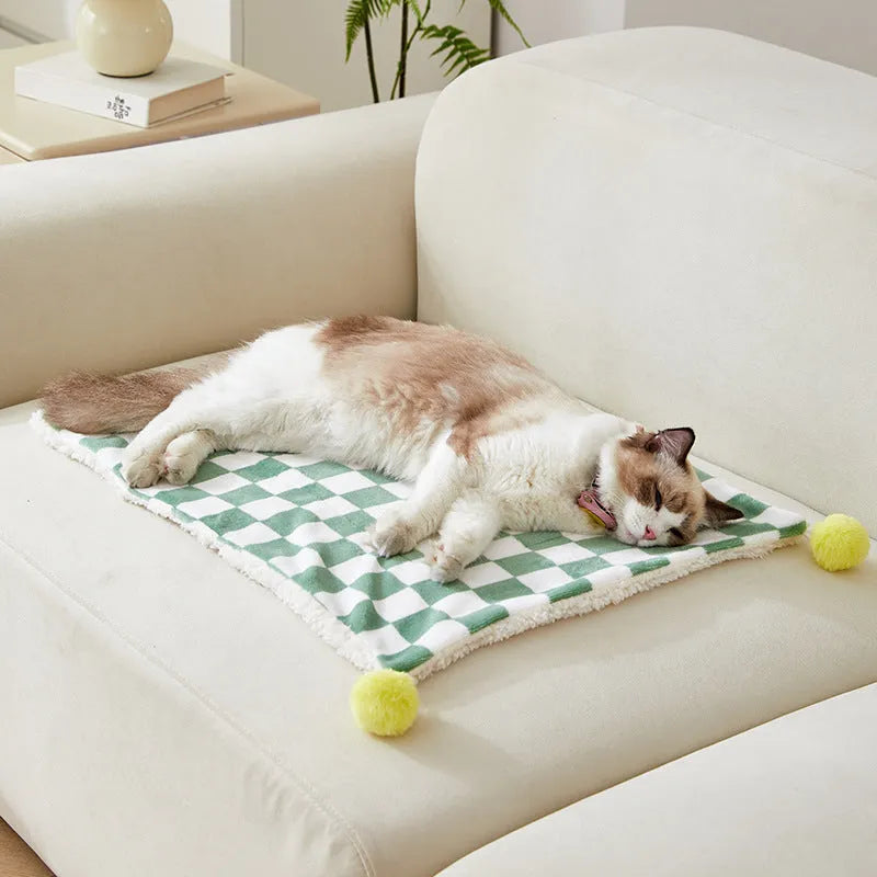 Green plaid pet fleece blanket with fur ball decoration on a sofa for a cat or dog.