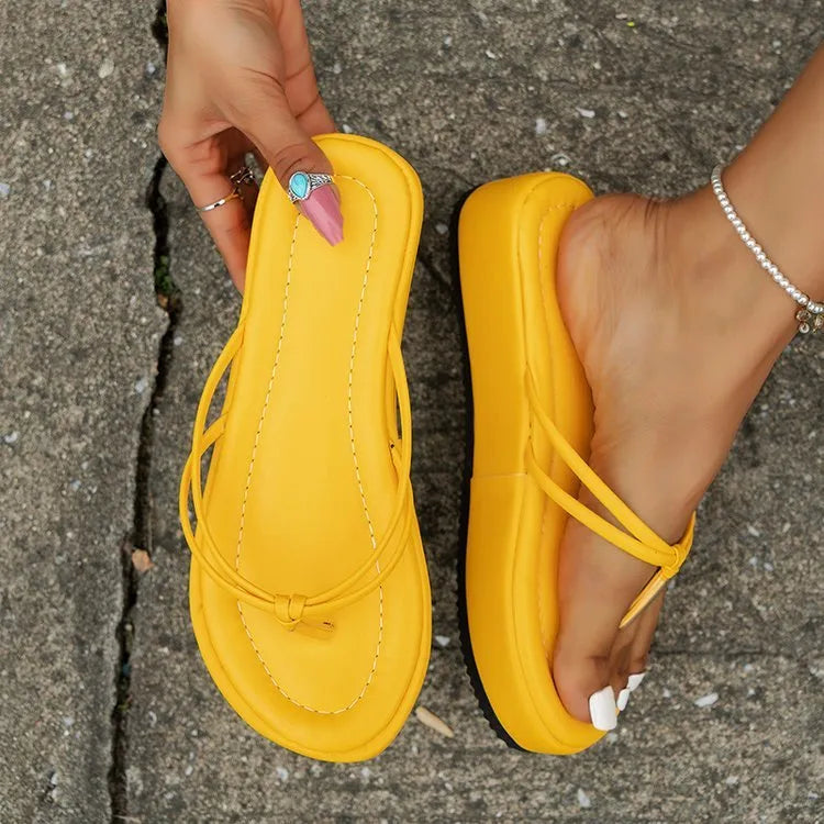 White thick-soled flip-flops with herringbone pattern PU upper and rubber sole on a sandy beach.