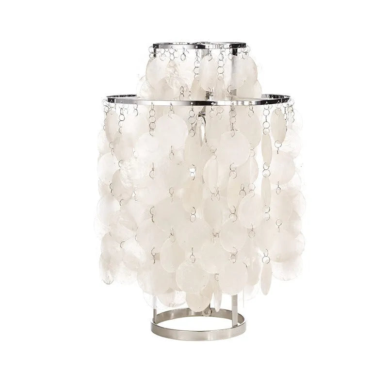 Modern bedside table lamp with a decorative white shell-shaped shade on a metallic chrome or gold base.