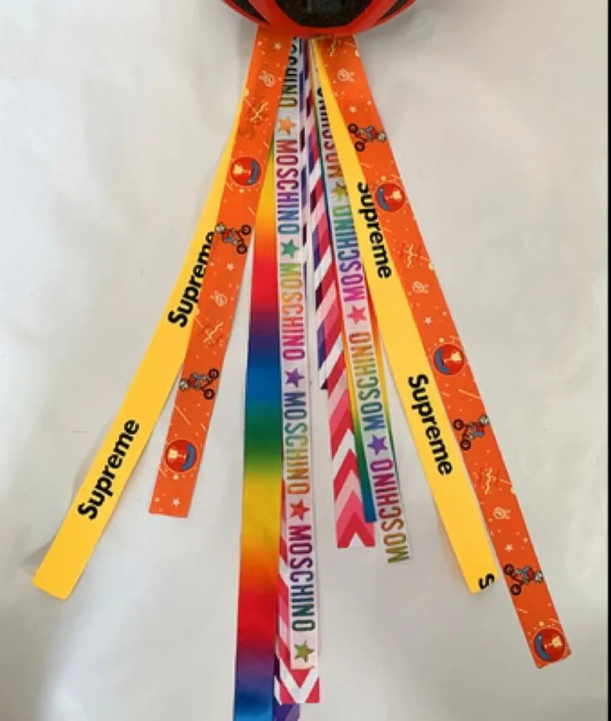 Colourful fabric helmet streamers for children's roller skating and ski helmets, shown in apricot, red, and grey.