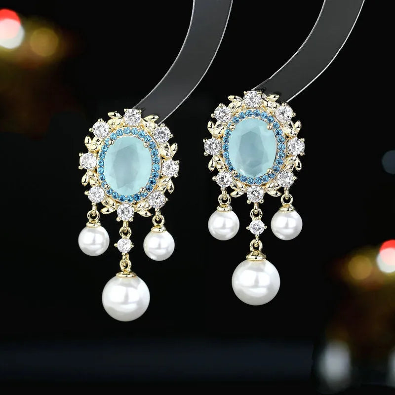 A pair of oval-shaped copper earrings with zircon inlay and a light-coloured pearl tassel.