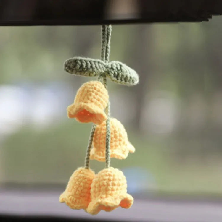 Green and white knitted wool car plant decoration with hanging rope on a car dashboard.