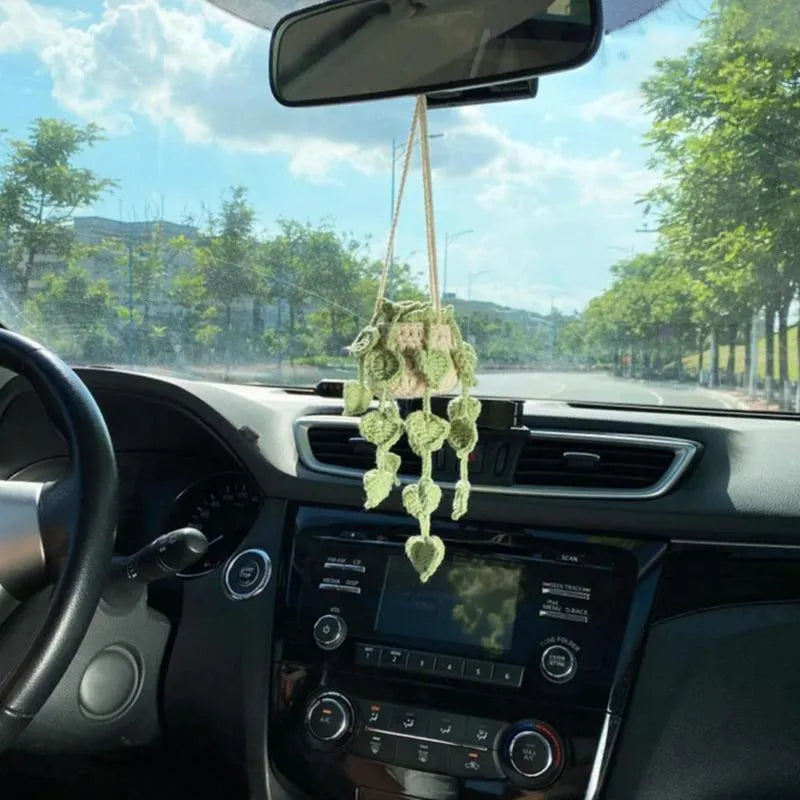 Green and white knitted wool car plant decoration with hanging rope on a car dashboard.