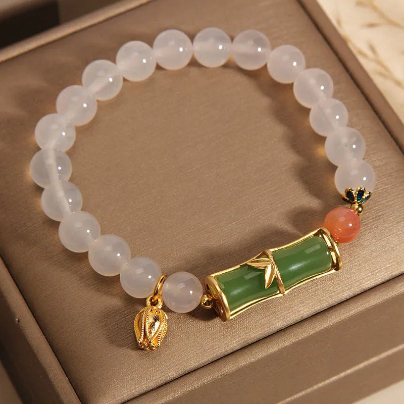 Close-up of a women's bracelet with a white agate jade bead and bamboo joint design on a natural background.