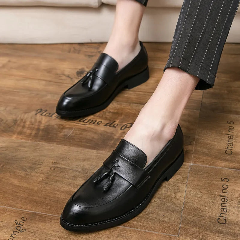Men's black tassel loafers with a slip-on design and rubber sole on a plain background.
