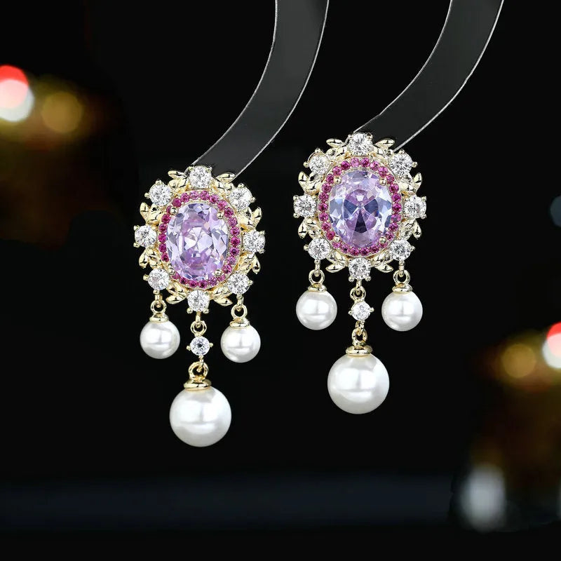 A pair of oval-shaped copper earrings with zircon inlay and a light-coloured pearl tassel.