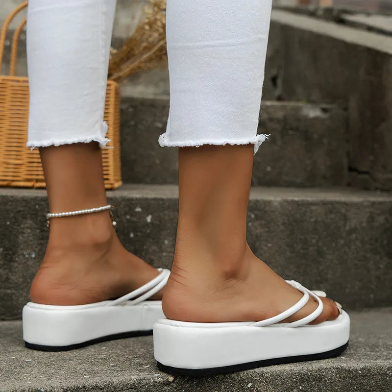White thick-soled flip-flops with herringbone pattern PU upper and rubber sole on a sandy beach.