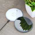 Black or white aluminium wireless charging pad showing soft LED light, for phones and headphones.