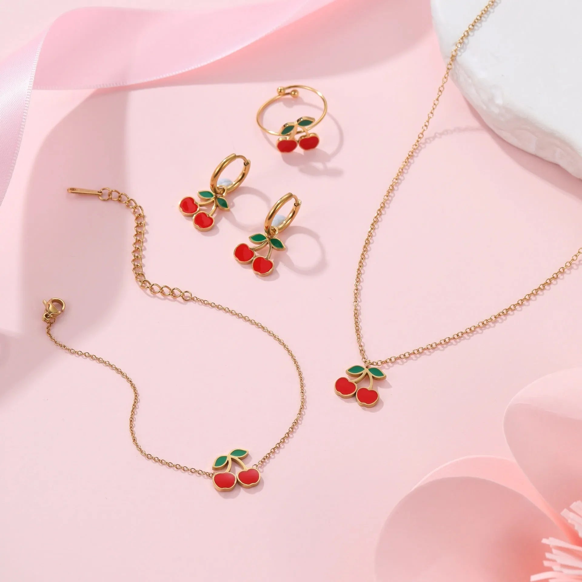 Four-piece stainless steel cherry jewellery set with gold plating: necklace, bracelet, earrings, and ring.