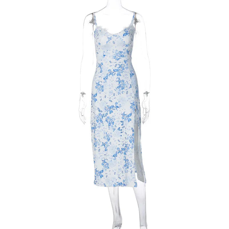 A woman wearing a long blue dress with a lace floral print, a side slit and thin suspender straps.