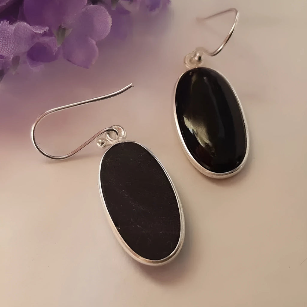 Oval black agate stone set in a geometric silver electroplated frame, forming a drop pendant earring for women.