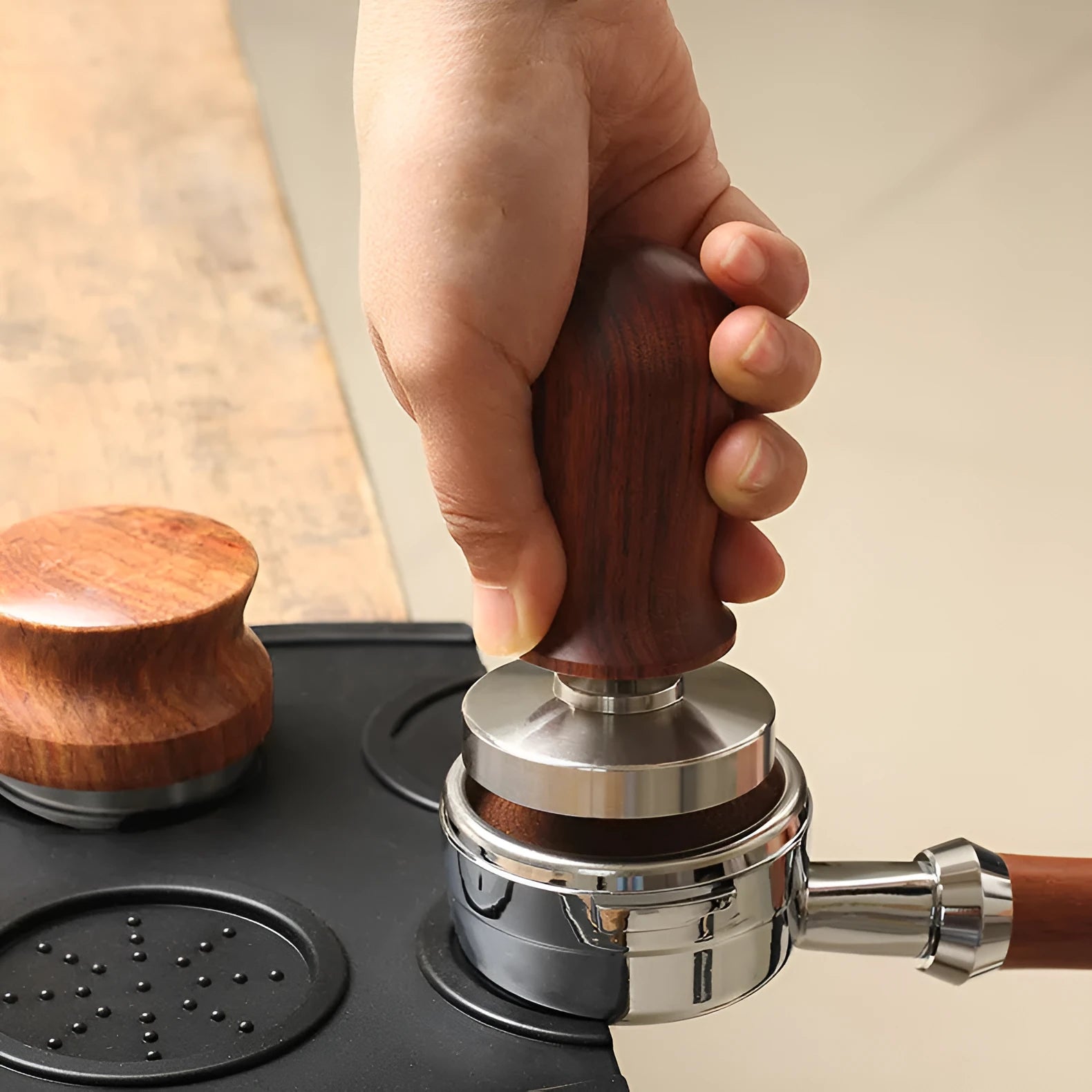 Black silicone pad coffee tamper with stainless steel base next to a red version on a counter.