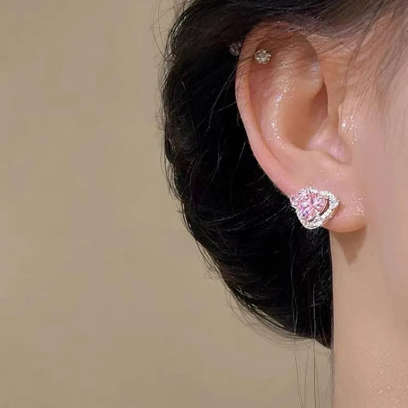 A pair of small white gold coloured heart shaped stud earrings for women on a jewellery card.