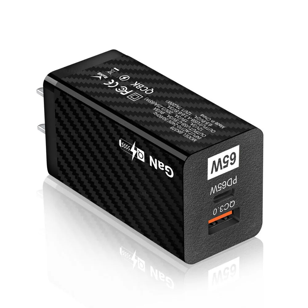 Compact black 65W GaN USB-C laptop charger with UK plug next to laptop
