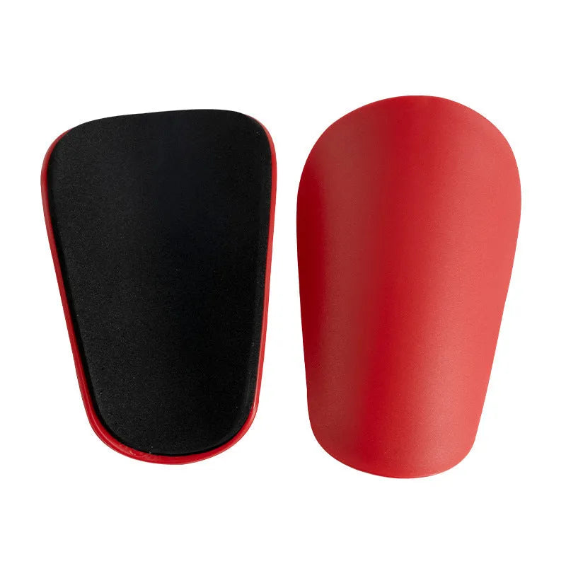 Two pairs of PU mini shin guards in black, white, red, and dream blue colours on a sports field.