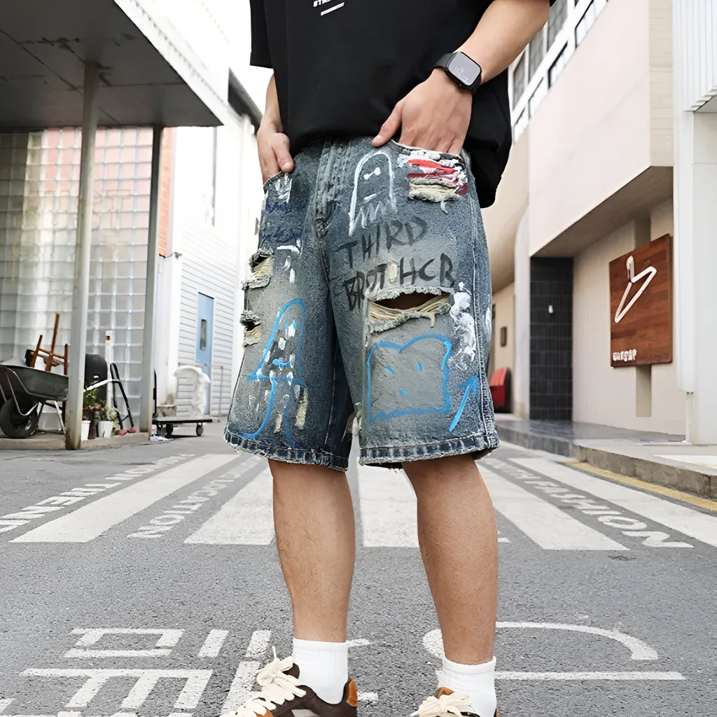 Blue men's ripped denim shorts with graffiti detailing and a straight-leg cut, showing front zipper fly.