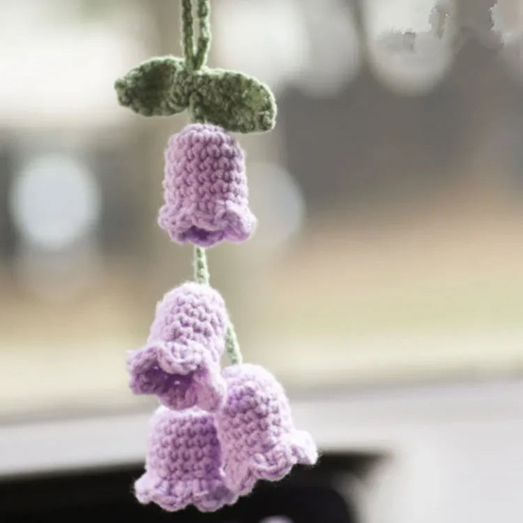 Green and white knitted wool car plant decoration with hanging rope on a car dashboard.