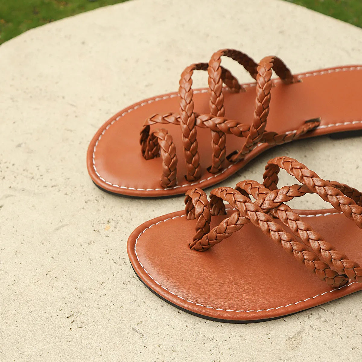 Women's brown woven clip-toe flat Roman sandal on a white background.