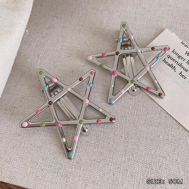 Two shiny silver metal duckbill barrettes with hollow star patterns on a plain background
