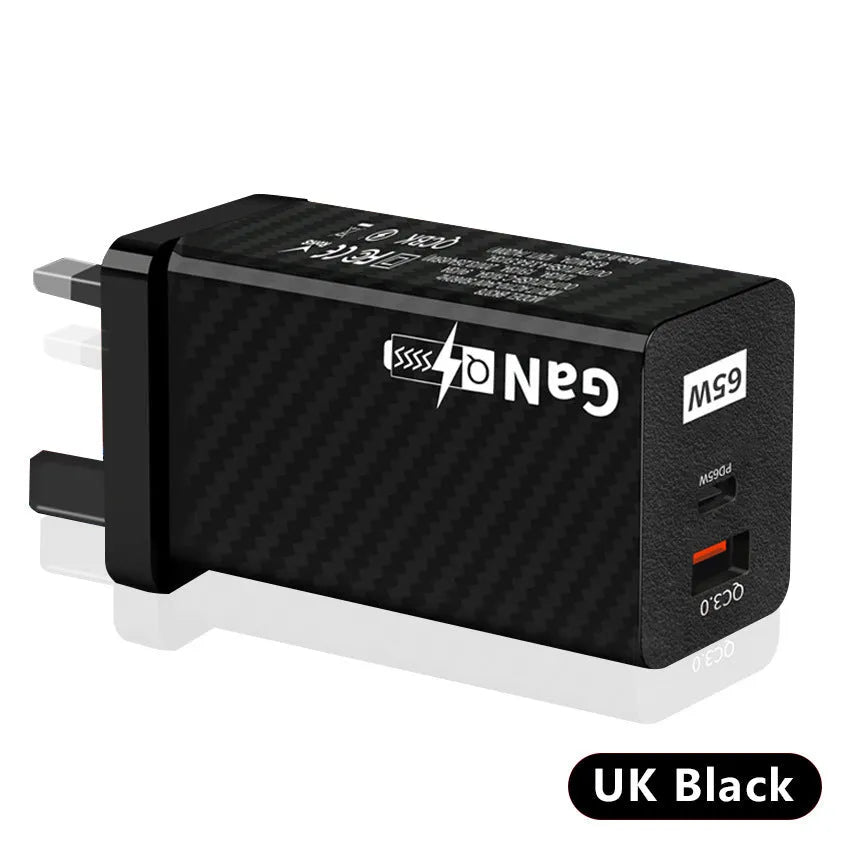 Compact black 65W GaN USB-C laptop charger with UK plug next to laptop